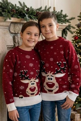 A boy and a girl in matching red Christmas sweaters with a reindeer pattern, smiling in front of the fireplace.