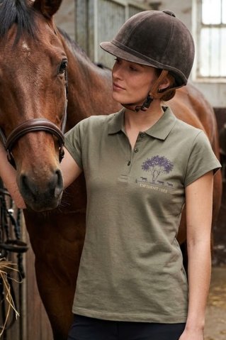 Mlada žena u zelenoj konjičkoj polo majici Ewident Horsesun u štali.