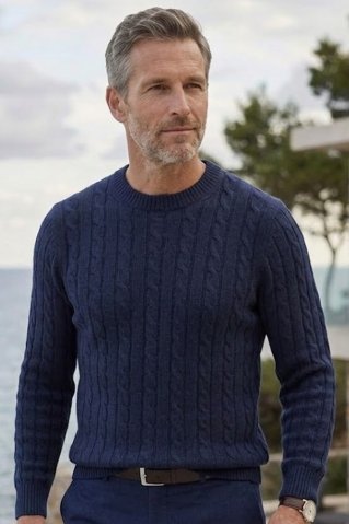 Muškarac u plavom pletenom puloveru stoji na terasi.