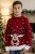 A young boy in a red Christmas sweater with a reindeer and snowflake pattern, standing in the living room next to a Christmas tree.
