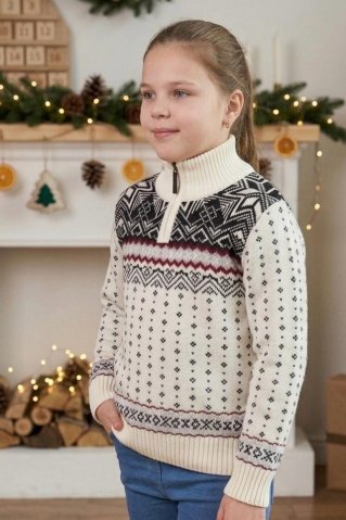 Boční pohled na dívku v bílém pleteném svetru s tradičním norským vzorem a zipem u krku ve vánočně zdobeném interiéru.
