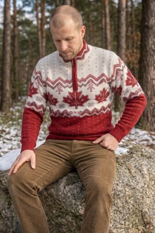 Man sitting on a rock in the forest wearing an Ewident men's sweater with a Norwegian maple leaf pattern